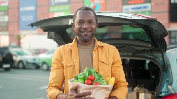 成熟したアフリカ系アメリカ人男性の笑顔とカメラのポーズ スタイリッシュな男が頭を上げてカメラを見る 野菜や果物が入ったエコバッグを持つ多文化男性 民族の多様性 — ストック動画