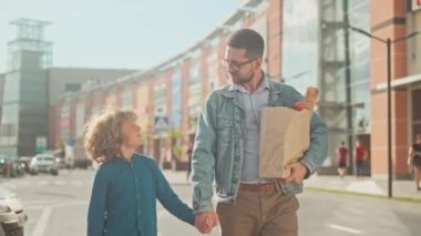 Baba, oğluyla el ele gidiyor. İnsan ve çocuk iletişim kurar ve göz teması kurarlar. Baba, poşetleri al ve oğlunla vakit geçir. Dükkanların arka planındaki çocuk ve baba otoparka gider..