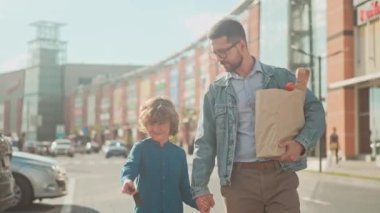 Baba ve oğlu yiyecek dükkanına alışverişe gittiler. Adam elinde poşet dolusu yiyecek tutuyor ve çocuğuyla canlı canlı konuşuyor. Çocuk anahtarla arabayı açıyor. Babam bagajı dikkatlice açıyor..