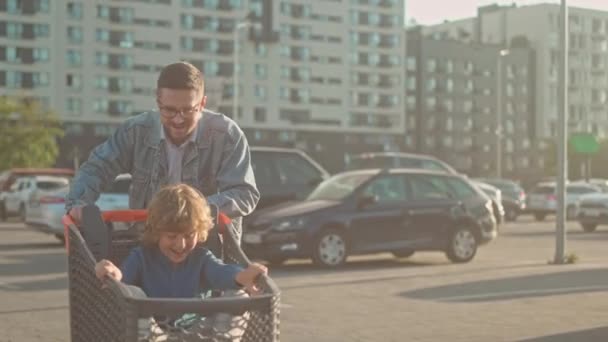 一个快乐的爸爸和儿子的画像父亲和儿子轮流开购物车 戴眼镜的男人和卷发男孩摆出姿势 微笑着 爸爸在城市和汽车的背景下和儿子玩得很开心 — 图库视频影像
