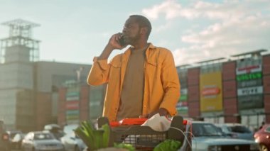 Afrika kökenli Amerikalı adam bir alet tutuyor ve telefonla konuşuyor. Bir sürü ürünü olan çok kültürlü bir erkek. Olgun adam dükkanların arka planında telefon görüşmesi yapıyor. Etnik çeşitlilik.