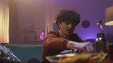 Genç adam evde dinleniyor. Genç adam kanepede oturuyor ve ağzına cips atıyor. Tatmin olmuş adam joystick 'i tutuyor ve video oyunları oynuyor. İçerideki ve günbatımındaki odada kıvırcık çocuk.
