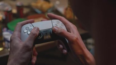 Yakın plan çekim. Adam elinde joystick tutuyor ve cips yiyor. Atıştırmalık ve içeceklerin arka planındaki genç adam. Gençliğin eğlence ve hobilerinin çeşitliliği. Tutkuyla oynayarak zaman geçirmek