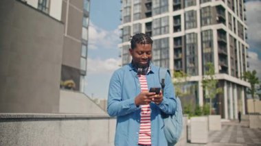 Açık havada dururken akıllı telefonunu kullanan çekici bir Afrikalı Amerikalı. Genç sakallı erkek, telefon tutarken kulaklık takıyor. Teknoloji cihazına mesaj yazıyor..