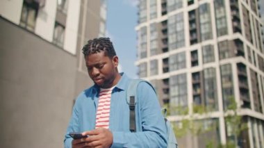 Sokakta telefonuyla gezen meşgul bir Afro-Amerikalı. Dışarıda akıllı telefon kullanan yakışıklı bir adam. Etrafa bakarken sensör ekranına dokunuyorum. Modern yaşam tarzı.