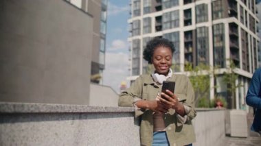 Güzel Afrikalı Amerikalı kadın dışarıda arkadaşlarıyla telefonda sohbet ediyor. Telefonuna mesaj yazarken gülümsüyor. Cihaz kullanırken sıcak kahve içmek. İyi hislerim var..