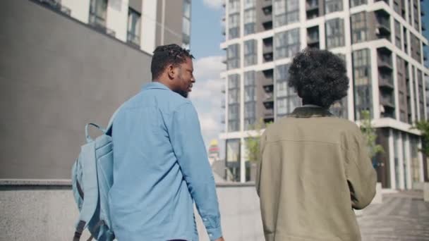 在室外摩天大楼旁边行走的非裔美国人的后视镜 有魅力的男人背着背包和他的女朋友聊着什么 穿过市区时喝热咖啡 — 图库视频影像