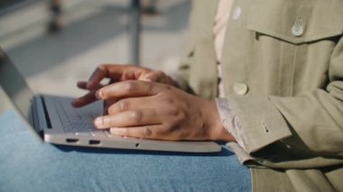 Kadınlar merdivenlerde otururken dizinde bulunan dizüstü bilgisayarın yan görüntüsü. Klavyeye mesaj yazmakla meşgul bir kız. Sokaktaki teknolojiyi kullanarak. İş yeri. Yaşam biçimi.