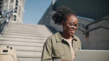 Diz üstü bilgisayarıyla çalışan gözlüklü güzel bir Afro-Amerikalı kadın. Aletini kullanırken lezzetli kahve içen mutlu kız. Merdivenlerde otururken iyi şeyler hissetmek..