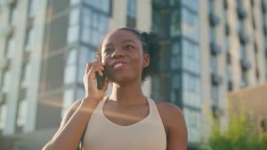 Akıllı telefondan konuşan Afro-Amerikan kadını yakından izleyin. Hafta sonu için plan yapıyorum. Uzağa bakıyorum. Arkadaki kızın arkasında güneş parlıyor. Olumlu tartışmadan gülümsüyor.