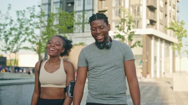 かわいいアフリカ系アメリカ人のカップルは 屋外で一緒に運動した後に歩きます 前向きに話し合うこと 幸せで疲れているように見える スポーツ用品を着用する — ストック動画