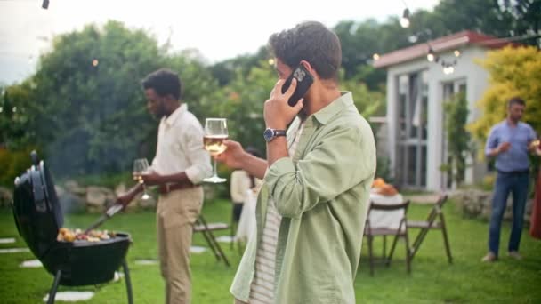 一个年轻英俊的男人拿着酒杯喝酒和敬酒 在朋友家的户外派对上 穿着休闲装 打电话 — 图库视频影像