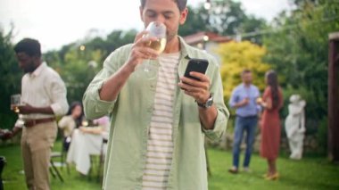 Olumlu adamın mesajlaşmasını, akıllı telefondan sohbet etmesini, gülümsemesini ve açık hava partisinde alkol içmesini kapatın. Tatil, tatil, yemek, insanlar ve yemek konsepti - arkadaşlar ev bahçesinde parti veriyor.