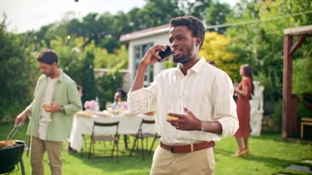 非洲裔美国人通过智能手机聊天 在自家院子里在线聊天 在家里的聚会上 一个年轻人喝着酒杯里的酒庆祝 手机和现代生活方式概念 — 图库视频影像