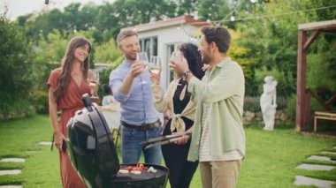 Izgara hazırlama, mangal tenceresi ızgarasında yanan kömür briketleri ev partisinde kadeh kaldıran ve içki içen bir grup arkadaş. Kutlama, boş zaman, yaz ve tatil kavramı.