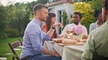 Yaz partisinde arkadaşlarıyla konuşan yakışıklı bir delikanlıyı yakından çek. Çok kültürlü arkadaşlar tost yapıyorlar, kutlama yapıyorlar, alkol içiyorlar, yemek yiyorlar, masada oturuyorlar, sıcak yaz gününün tadını çıkarıyorlar..