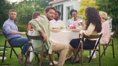 Kamera dışarıda yaz partisinde günlük giysiler içinde yakışıklı, neşeli bir adama geçiyor. Karışık ırklar mutlu genç erkekler ve kadınlar parti masasında içki içip gülüyor ve kadeh kaldırıyorlar..