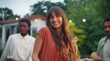 Arkadaşlarıyla çemberin merkezinde dans eden, ilgi gösteren ve kameraya bakan güzel bir kadın. Yaz zamanı, evin önündeki bahçede dans partisi. Kutlama, müzik, neşe ve eğlence.