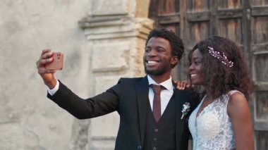 Afrikalı Amerikalı çift eski binanın önünde dikilirken telefonla fotoğraf çekiyorlar. Genç koca selfie çekerken karısına sarılıyor. İnsanları sevmek, gülümsemek ve mutlu olmak..
