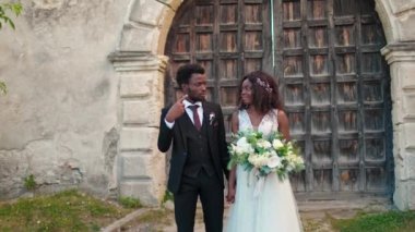Nikah töreninden sonra kiliseden yürürken gelinlik giyen Afrikalı genç bir çift. Yakışıklı koca güzel karısıyla konuşuyor. Kutlama konsepti.