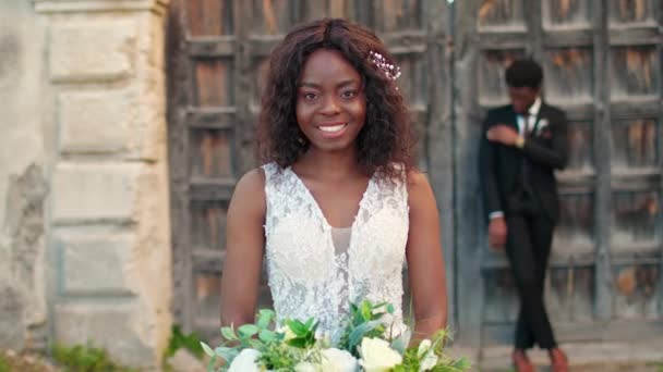大きい花束を保持する素晴らしいウェディングドレスを持つ若いアフリカ系アメリカ人の花嫁 満足した女性が結婚式を始める準備をします 背景で魅力的な婚約者は彼の愛する女性を待っています — ストック動画