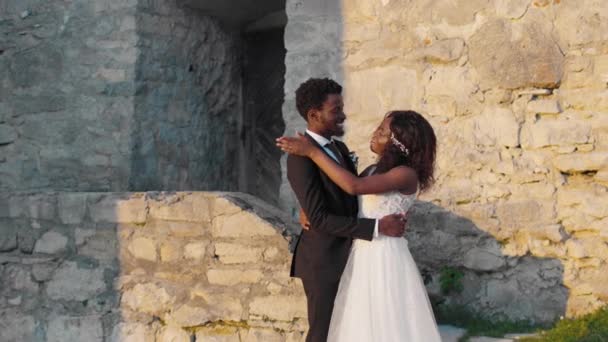 爱穿着婚纱的非洲裔美国人夫妇 同时彼此做出承诺和承诺 快乐的新郎在户外石头城堡附近拥抱他漂亮的未婚妻 欢乐日 — 图库视频影像