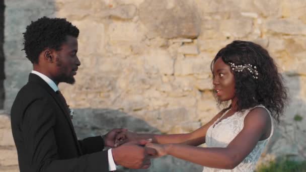 非洲裔美国人情侣在外面的石楼附近拥抱 漂亮的未婚夫穿着白色婚纱拥抱他可爱的新娘 新婚夫妇之间的爱情和激情 结婚的概念 — 图库视频影像
