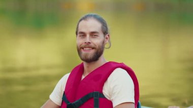 Gölde yüzen kırmızı yelek giyen sakallı beyaz adamın portresi. Rahatlama sırasında iyi şeyler hissedersin. Kameraya neşeyle gülümsüyor. Suyun üzerinde eğlenmeyi seviyorum. Açık havada..
