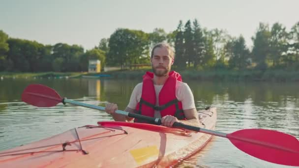 湖のボートに座っている間 安全ベストを保持している魅力的なコーカサス人男性 大きな池でカヌーを練習する準備をする 背景に見える森林 晴れた日 バケーション — ストック動画
