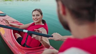 Kano üzerinde yüzerken can yeleği giyen at kuyruklu mutlu beyaz kadın. Genç bayan kürek çekiyor ve teknede otururken erkek arkadaşıyla konuşuyor. Boş zaman. Seyahat kavramı.