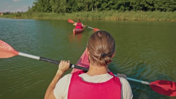 カヤックの女性の後ろで泳ぐ男のリアビュー 晴れた日に湖で休む 一緒にカヤックをするベストの人たち レクリエーション リバー トリップ 美しい風景 観光コンセプト — ストック動画