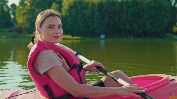 ボートに座っている間 美しい白人女性の側面の景色 カメラで笑顔の赤いベストを着ている女性 アウトドアで休む 湖でカヤックをする 素晴らしい自然の景色 — ストック動画