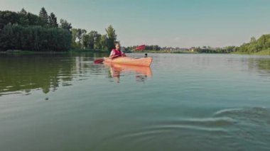 Genç adam yaz günü kano yapıyor. Aktif olarak sandalda otururken kürek çekiyor. Antrenman kanosu. Yaz tatili. Orman zeminli büyük bir göl. Nehir suyunda dinleniyorum. Su sporları.