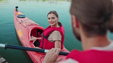 Güzel beyaz bir kıza kürek çeken bir adamın dikiz görüşü. Gölde teknede otururken mutlu bir şekilde gülümseyen kırmızı yelek giyen tatlı bir kadın. Kanoya hazırlanıyorum. Yaz günü. Doğadaki macera.