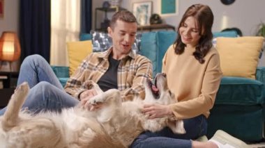 Mutlu Kafkasyalı koca ve tatlı karısı oturma odasında sevimli tüylü köpeğini okşuyor. Dili kadın bacakları üzerinde dinlenen rahat bir köpek. İletişim kuran ve birlikte iyi vakit geçiren insanlar..