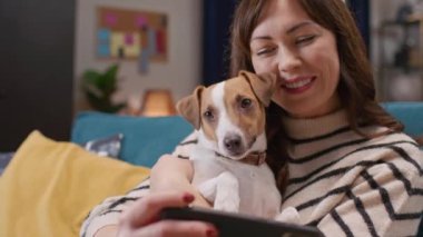 Güzel beyaz kadın akıllı telefon kullanırken sevimli köpeğine sarılıyor. Sevgili bayan sahibi telefonda Jack Russell 'ıyla fotoğraf çekiyor. Komik köpek sensör ekranında yansımasına bakıyor..