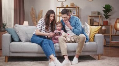 Eşim ve kocam kanepede kızımla oturuyor. Evli bir çift ve kızı telefonda korkunç videolar izliyorlar. Akıllı telefonlara bakan genç bir aile. Ebeveynler ve küçük kızları evde dinleniyorlar..