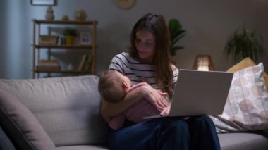 Gece geç saatlere kadar çalışan bir kadın. Annem doğum iznindeyken internette çalışıyor. Kızı tutan ve dizüstü bilgisayarla çalışan bir kadın. İnternette çalışmak için dizüstü bilgisayar kullanan kadın. Bebek elleri üzerinde uyuyor..