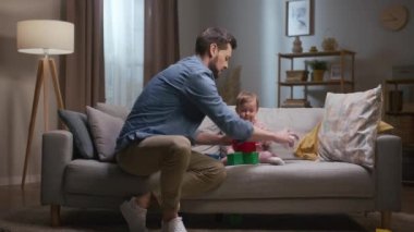 Baba küçük kızıyla vakit geçiriyor. Küçük kız yere renkli küpleri fırlatıyor. Babam renkli küplerden kule inşa ediyor. Çocuk oyuncağıyla oynayan bir adam. Babam el çırpıyor.