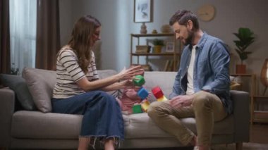 Genç ebeveynler geceyi küçük kızlarıyla geçirirler. Neşeli bir aile kanepede oturuyor. Anne ve baba renkli küplerden bir kule inşa ediyorlar. Yeni yürümeye başlayan çocukla iyi eğlenceler. Ebeveynler el çırpıyor.