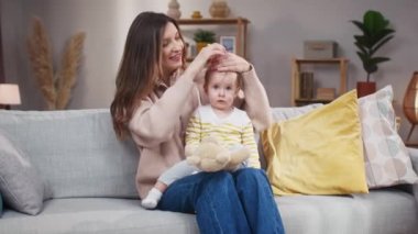 Gözlerini ovuşturan uykulu kız. Annem kısa kız saçlarıyla kuyruk yapmaya çalışıyor. Anne ve bebeğinin tuhaf bir eğlencesi. Anne ve çocuk evde birlikte vakit geçiriyorlar. Güzel çocuk, dizlerinin üstünde oturuyor.,