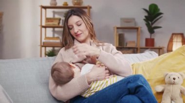 Kanepede oturan ve bebeği sallayan kadın. Anne küçük kıza ninni söylüyor. Anne bebeğini emziriyor. Küçük kızı uyutan bir kadın. Bir kadın bebeğini başından okşuyor..