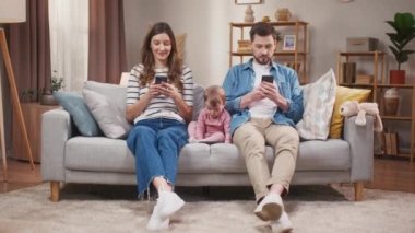 Cihazlara bağımlı gençler. Ebeveynler neşeli bir şekilde telefon oyunları oynuyorlar. Cep telefonuyla çizgi film izleyen küçük bir kız. Sanal internet dünyasında vakit geçiren genç bir aile.