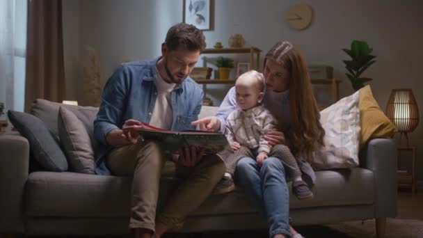 Pequena Menina Leitura Livro Com Pais Família Feliz Sentada Sofá — Vídeo de Stock