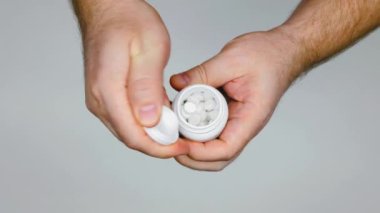 Hands open a vial of pills and man pouring many white pills from a pill vial into his palm. Plastic Medicine Pill Bottle for Prescription Medication. Medic Pharmaceutical Container. Top view. Close-up