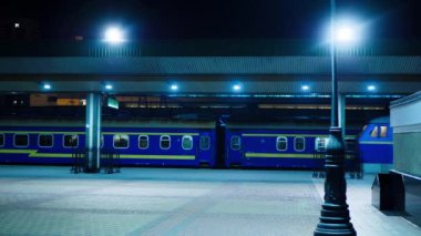 Train and passenger cars at the railway station. Illuminated by bright lights, railway station and the cobbled square. Colorful sleeping wagons with people. Transportation and delivery of travelers