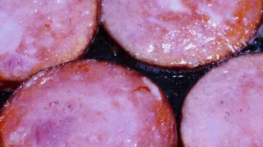 Sausage is fried in a pan. Pork meat is cooked in olive oil. Beef sausages are fried in boiling vegetable oil. Cooking meat products on the stove in the kitchen. Production of fried sausages. Close-up