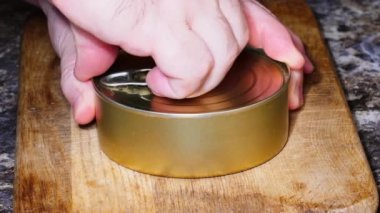 Opening a can of pate. Male hands open a tin can with a key with a liver pate. Canned meat on a wooden board on the background of the kitchen table. Close-up. Side view. Canned processed meat product