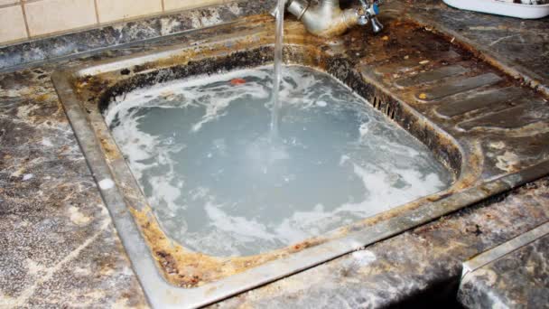 汚れた台所の流しの汚れた水 泥だらけの石鹸水は古い台所の流しにあふれている 水は蛇口から食品廃棄物を含む非常に汚染された液体に注ぐ キッチンには掃除が必要だ — ストック動画