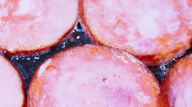 Yağda kızartılmış sosis. Kaynayan zeytinyağında kızartılmış halkalar halinde kesilmiş et sosisi. Domuz eti, sığır eti ve tavuktan yapılmış pembe sosis. Sıcak yağ ateşte köpürüyor ve mutfakta pişirmeye hazır.